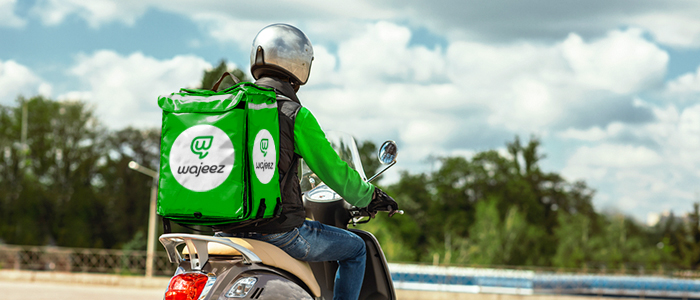 A delivery man riding his scooter with a green Wajeez box on his back.